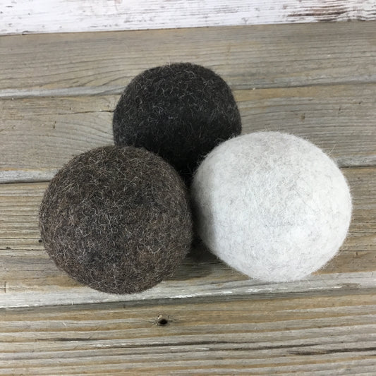 Three different colored alpaca dryer balls placed on a wooden surface.