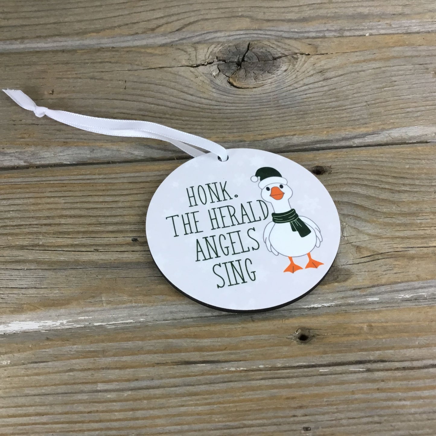 Round ornament with a cartoon goose and text on a wooden surface