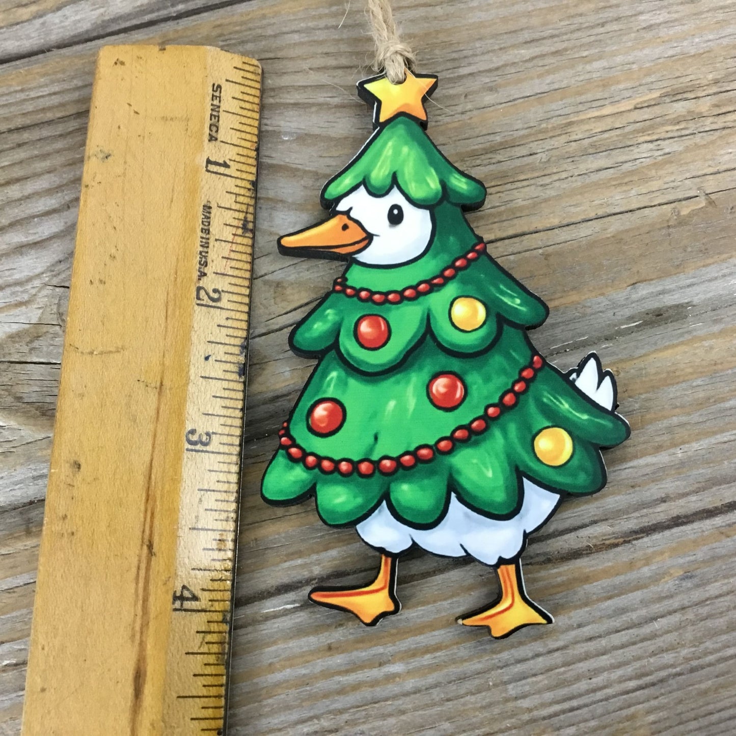 Decorative Christmas tree-shaped ornament with a goose face, hanging on a wooden surface next to a ruler.