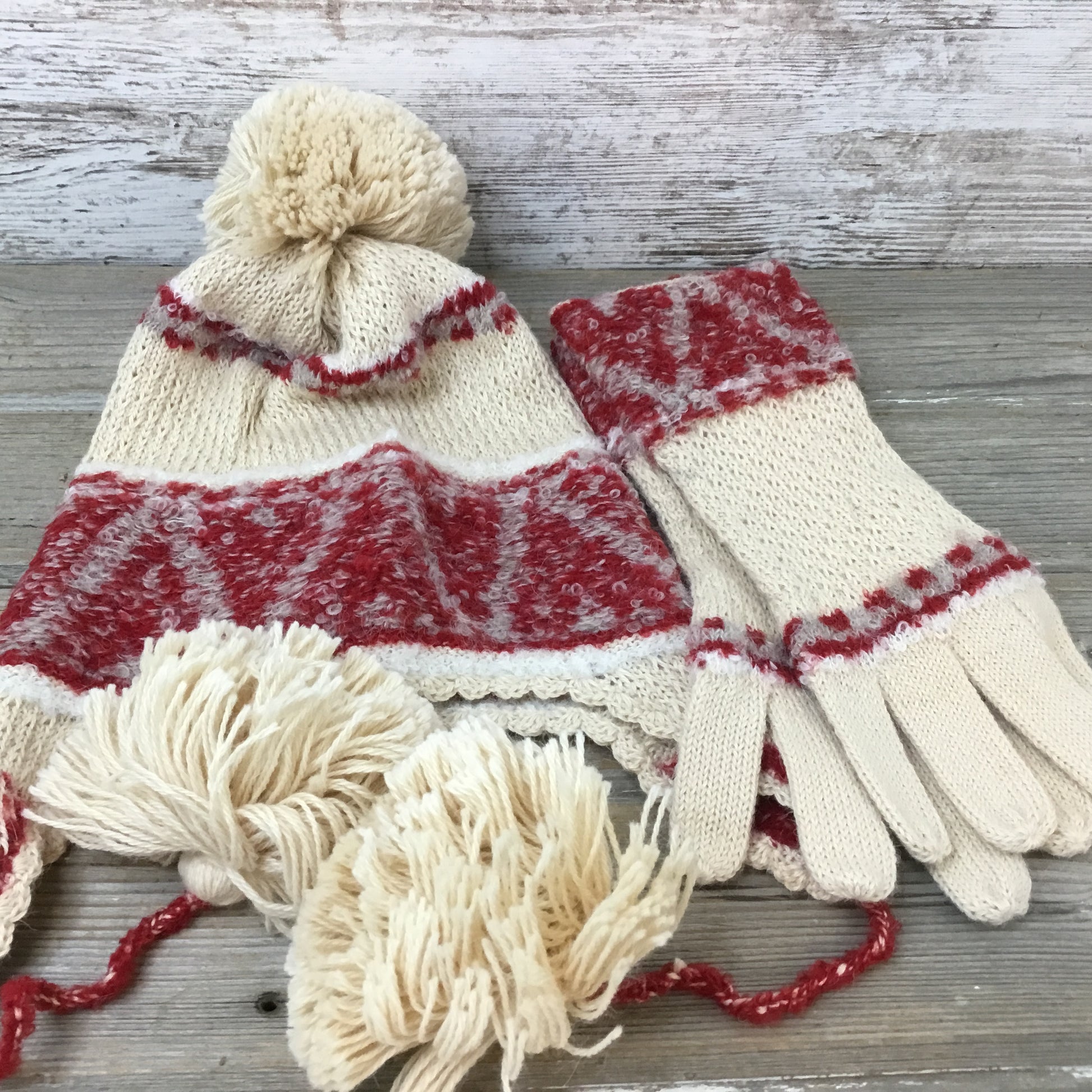 A set of beige and red patterned alpaca wool gloves and a hat with tassels on a wooden surface.
