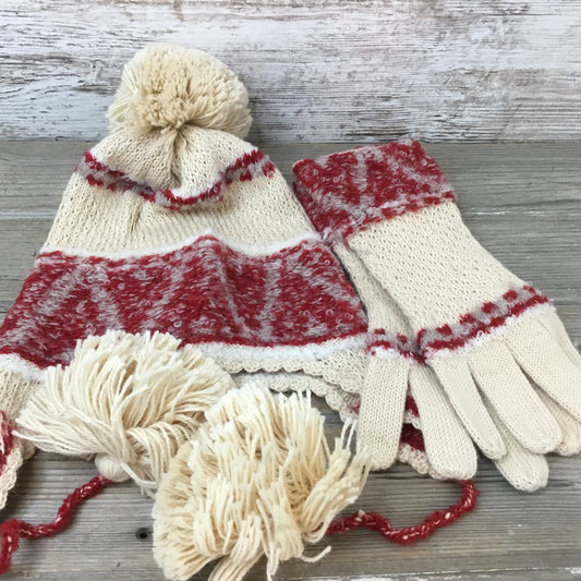 A set of beige and red patterned alpaca wool gloves and a hat with tassels on a wooden surface.