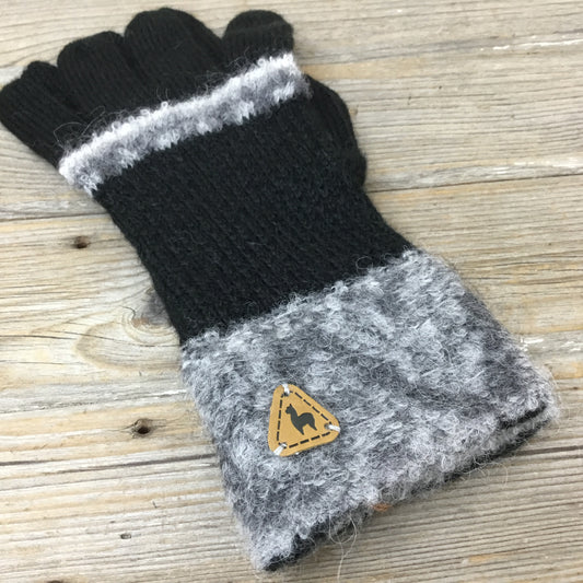 A pair of handmade Alpaca gloves with boucle knitted textures and Shipibo patterns, predominantly black and gray in color, displayed against a wooden background.