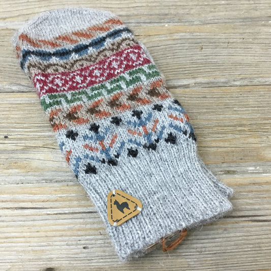 A pair of multicolored knitted alpaca mittens on a wooden surface.