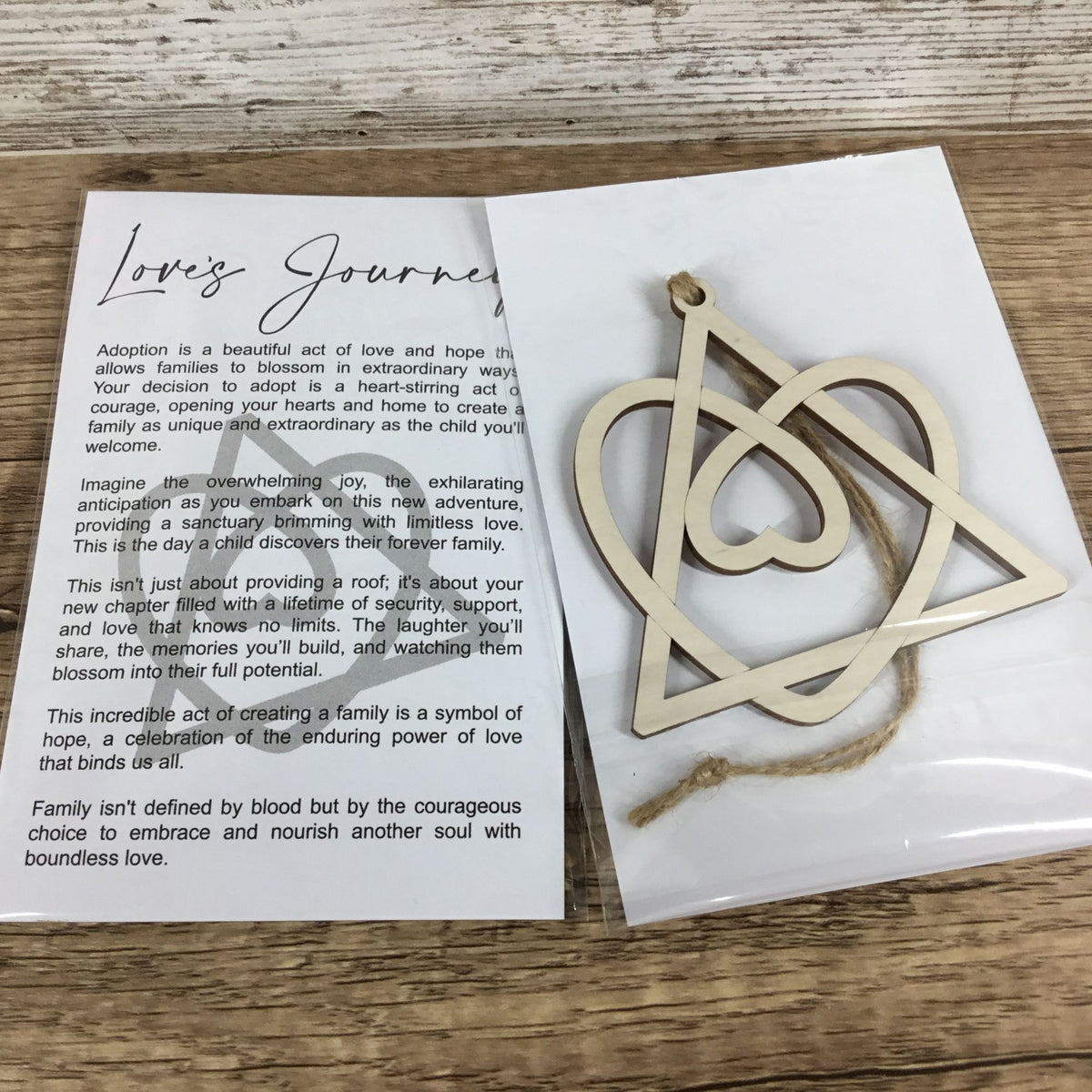 A wooden cutout ornament with a hanging loop, displayed next to a printed adoption card on a white sheet over a wood surface.
