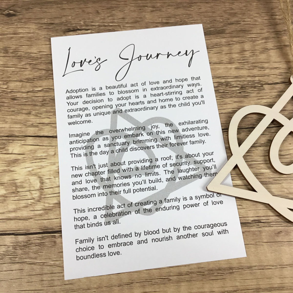 A printed adoption journey card with black script and body text, styled on a wooden surface 