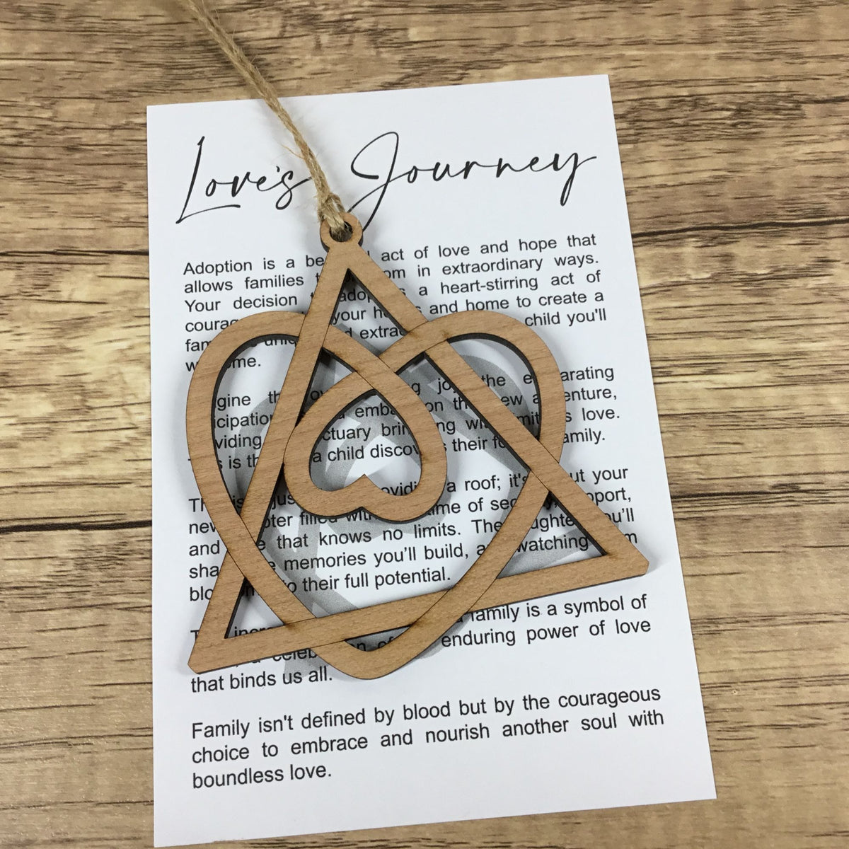 A light natural wood carved ornament shaped like the interconnected family symbols, hanging from a string over a printed card on a wooden tabletop.