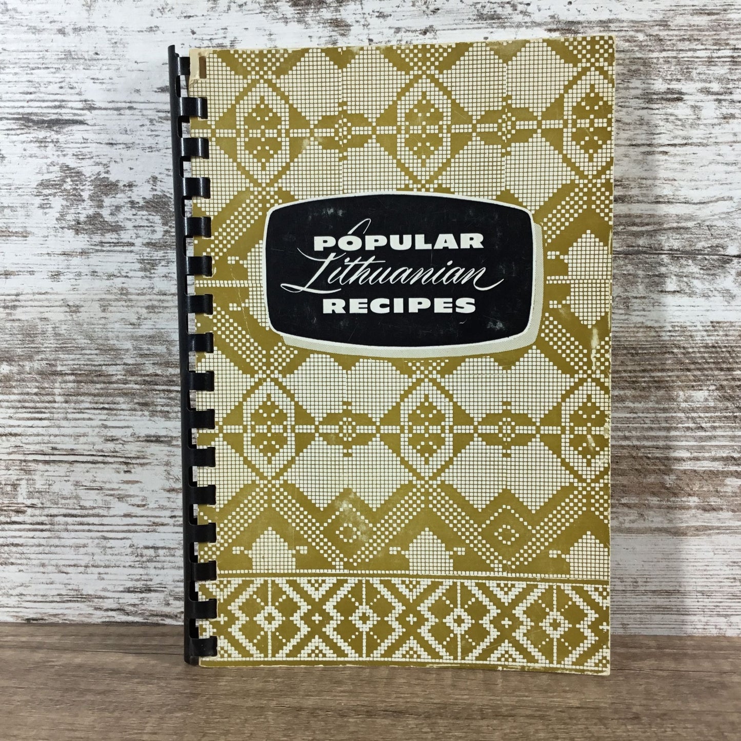 Cookbook titled 'Popular Lithuanian Recipes' with geometric pattern on wooden surface