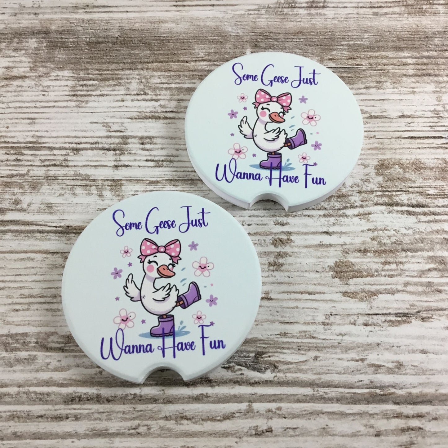 Two white coasters with a cartoon goose and text on a wooden surface