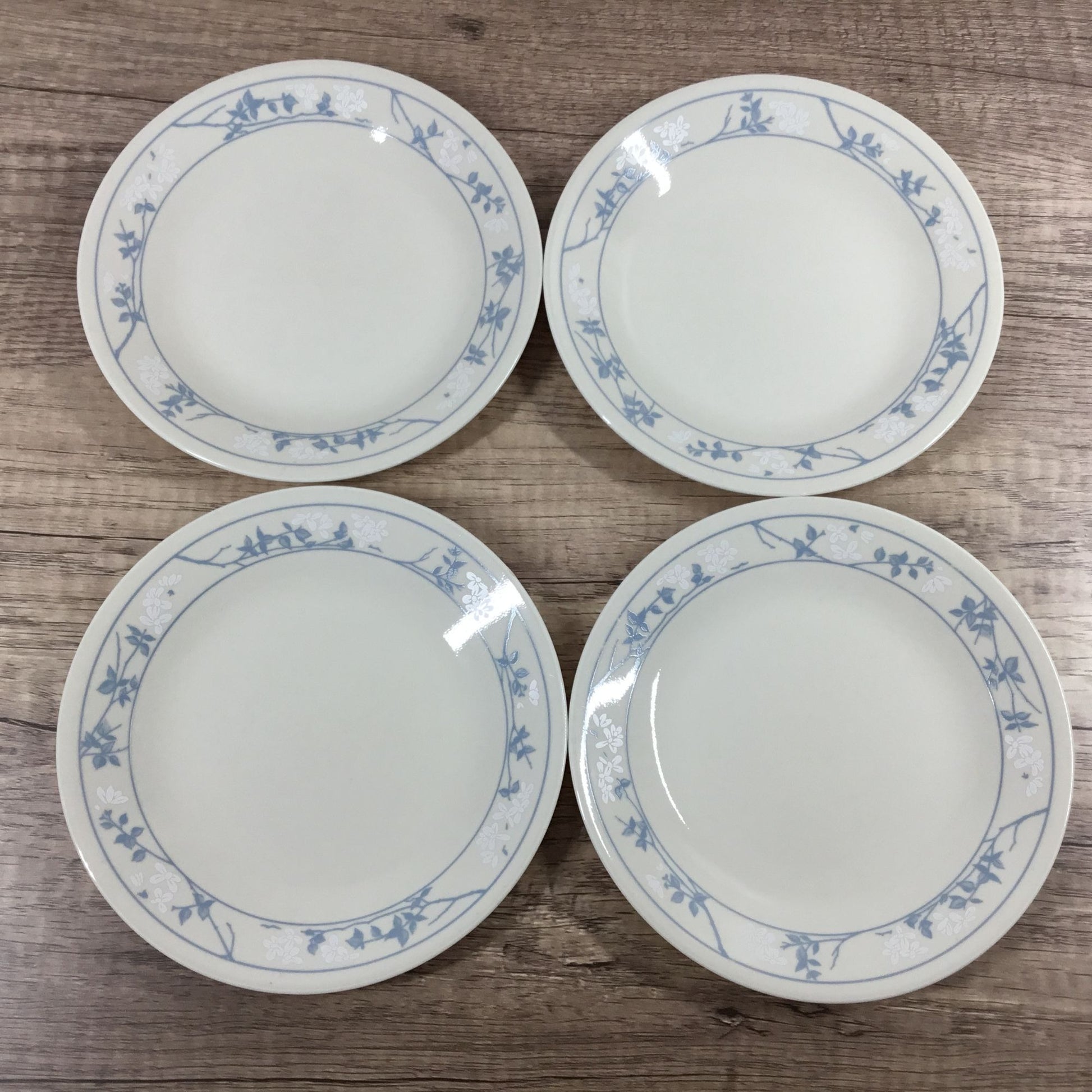 Four white Corelle plates with a blue and white floral border pattern, arranged on a wooden surface.