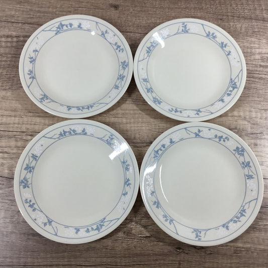 Four white Corelle plates with a blue and white floral border pattern, arranged on a wooden surface.