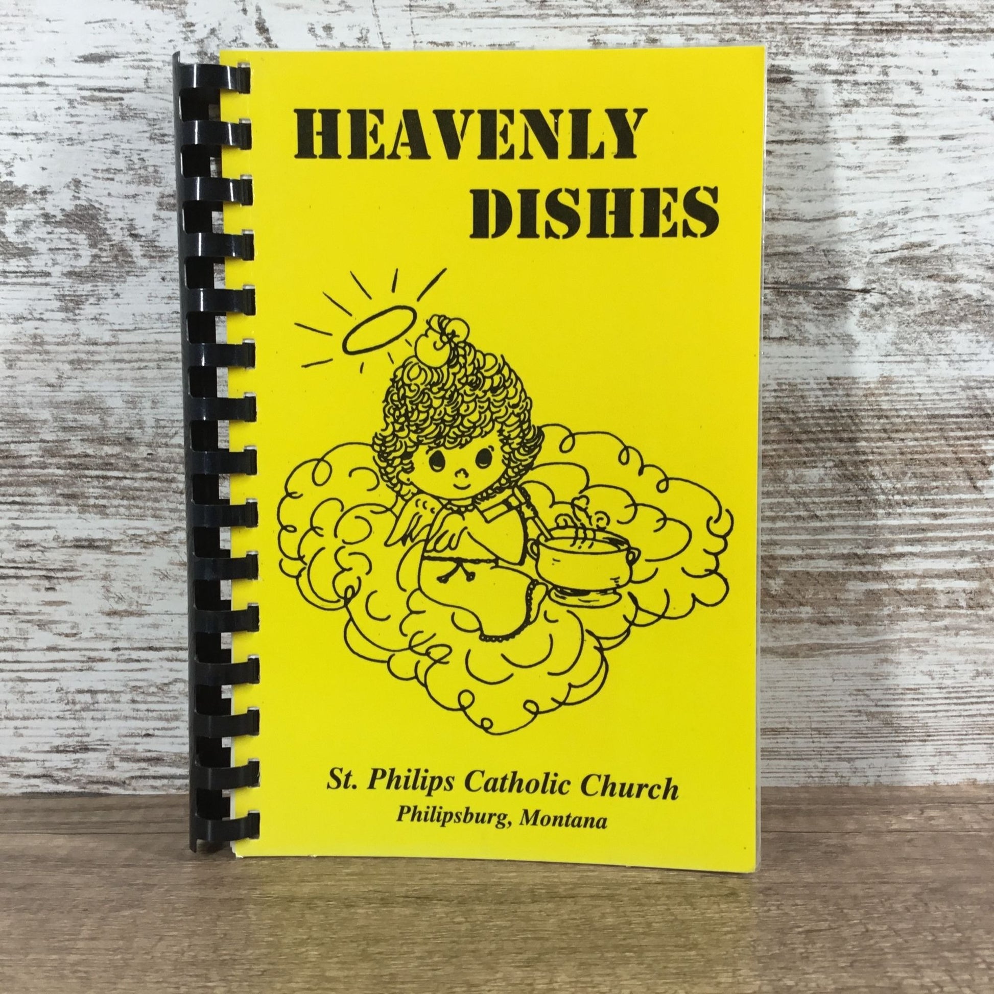 Notebook titled 'Heavenly Dishes' from St. Philip's Catholic Church on a wooden surface.