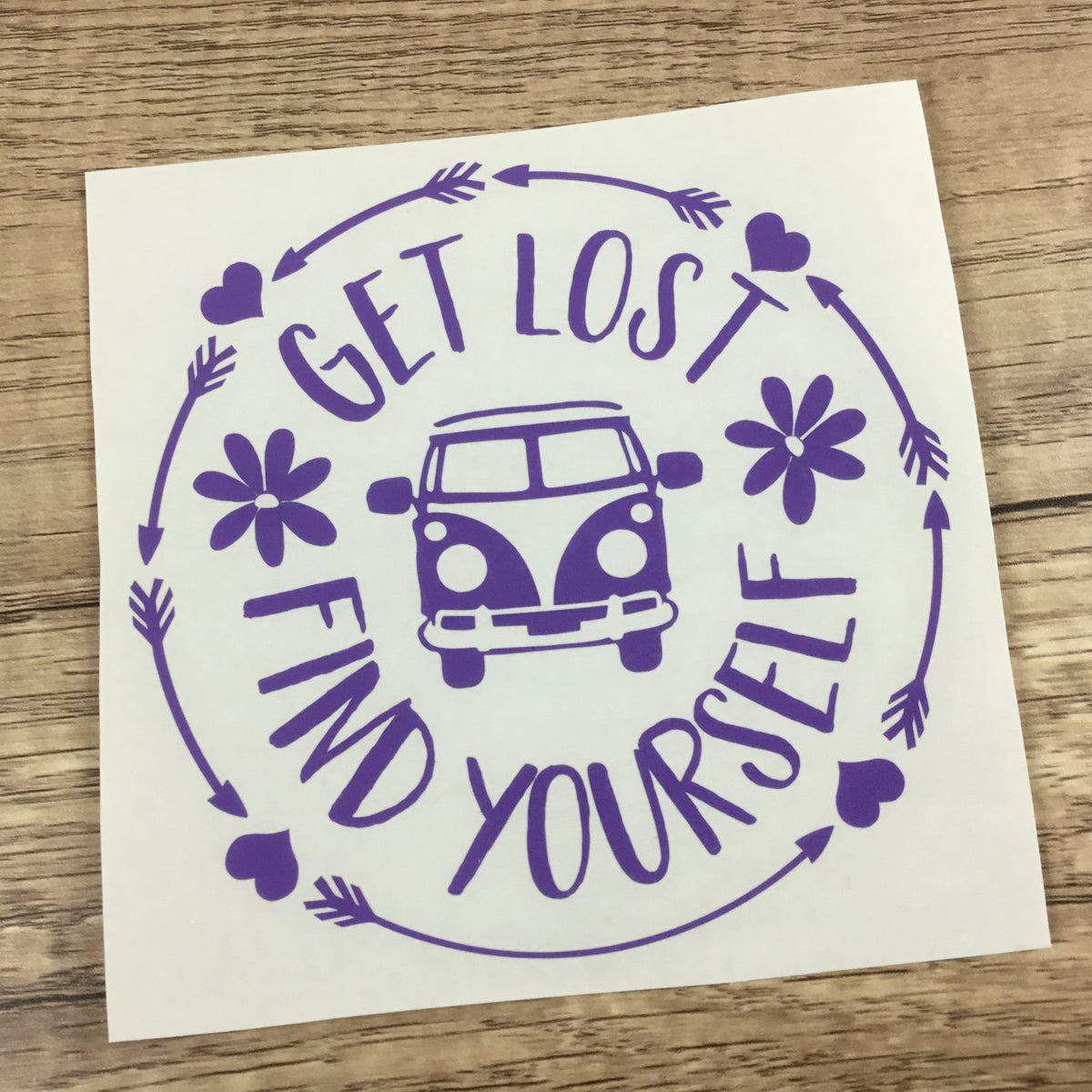 A decal sheet featuring a purple graphic design with the words 'GET LOST FIND YOURSELF' around a retro van, hearts, flowers, and arrows, shown on a wooden surface.