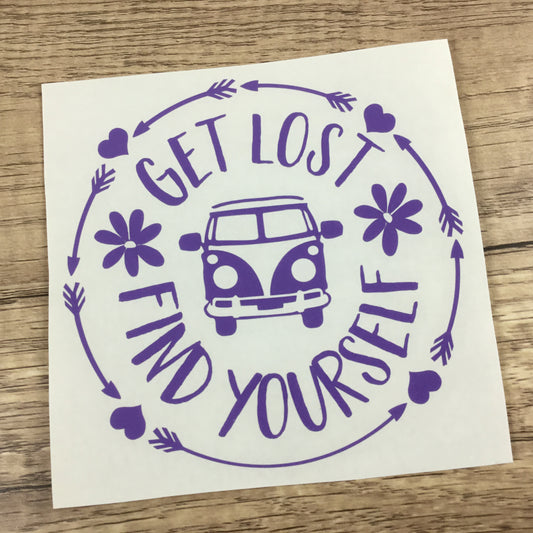 A decal sheet featuring a purple graphic design with the words 'GET LOST FIND YOURSELF' around a retro van, hearts, flowers, and arrows, shown on a wooden surface.