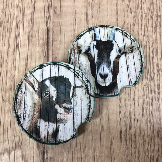 Two round car coasters featuring a rustic wood-plank design with a black and white goat portrait, displayed on a light brown wood-grain surface.