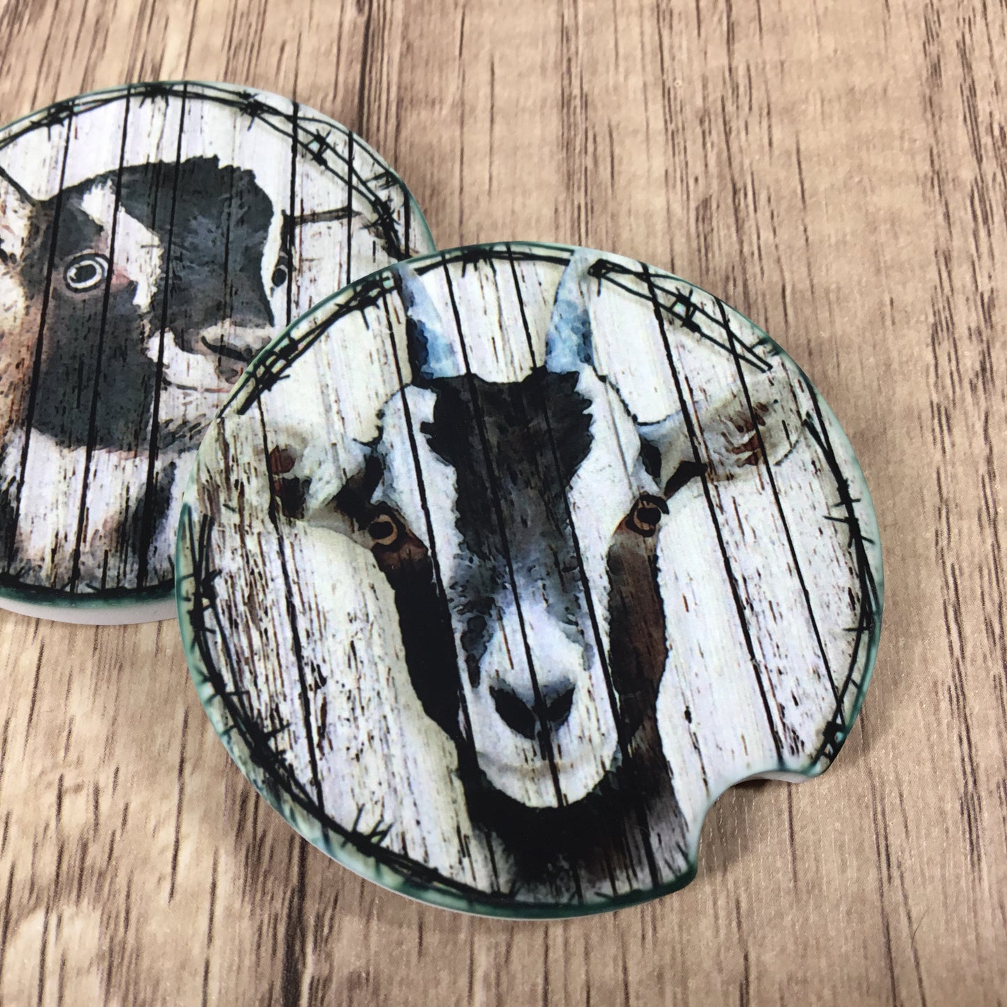 Two round coasters with a rustic goat print, displayed on a light brown wood grain surface.