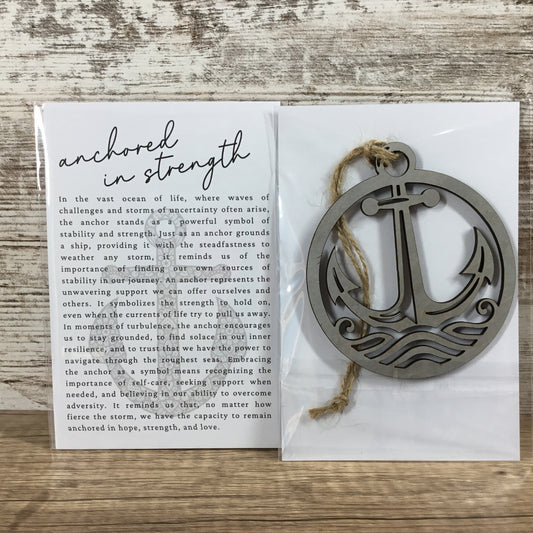A wooden anchor ornament with a natural wood bail and a twine hanger, displayed on a white card that reads 'anchored in strength' with a quote, set on a rustic wood background.