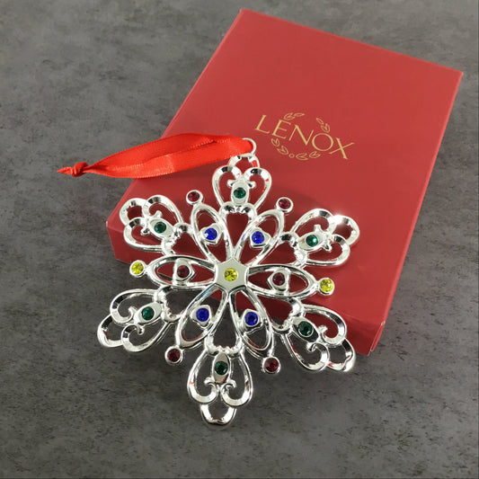 Decorative snowflake ornament with colored gemstones on a Lenox branded red box.
