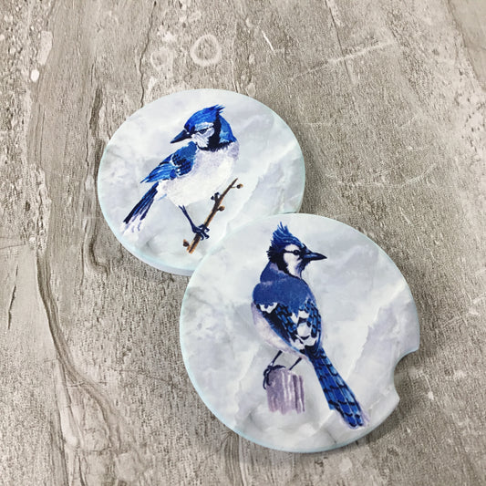 Two round car coasters with blue jay designs on a textured surface