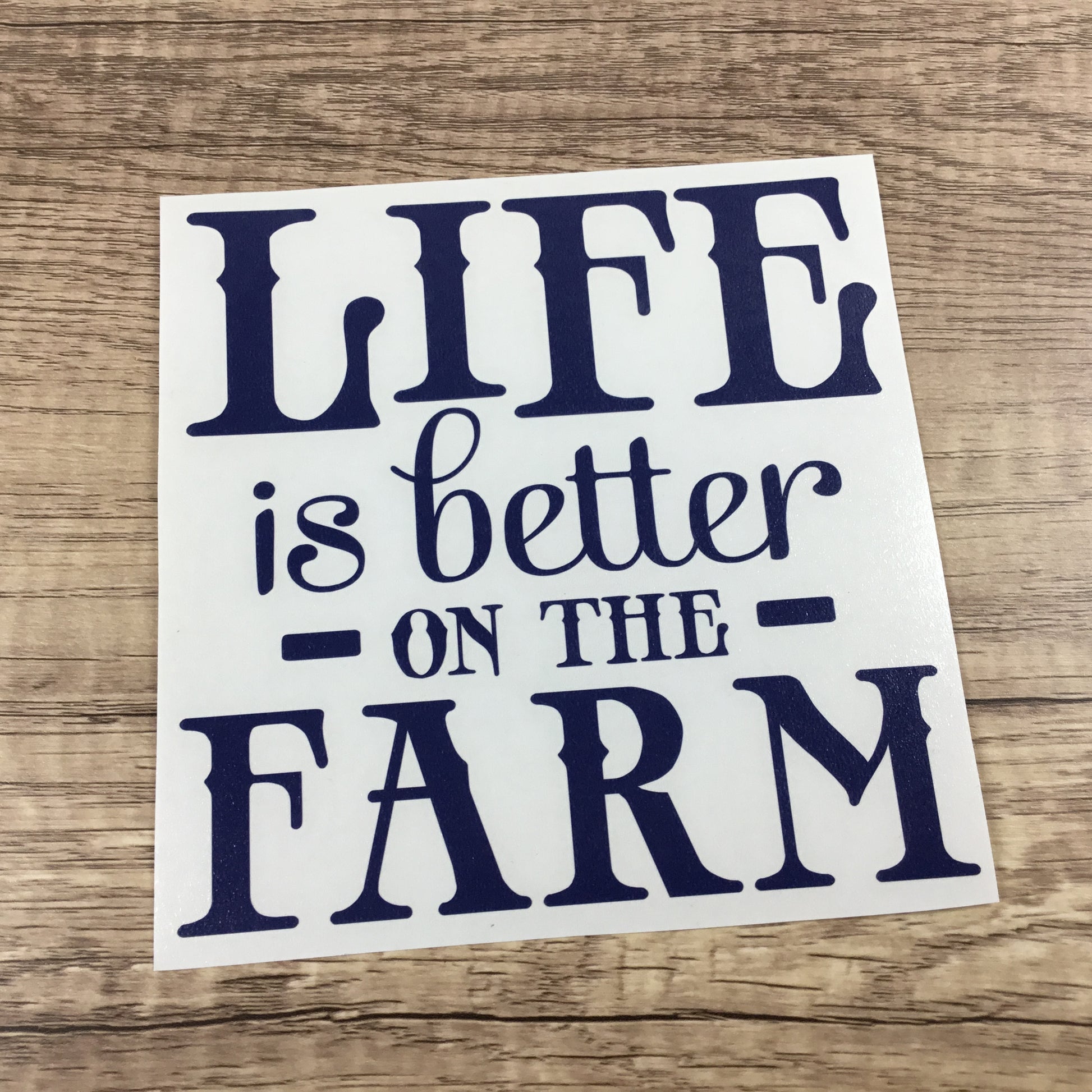 Sticker with 'Life is better on the farm' text on a wooden surface