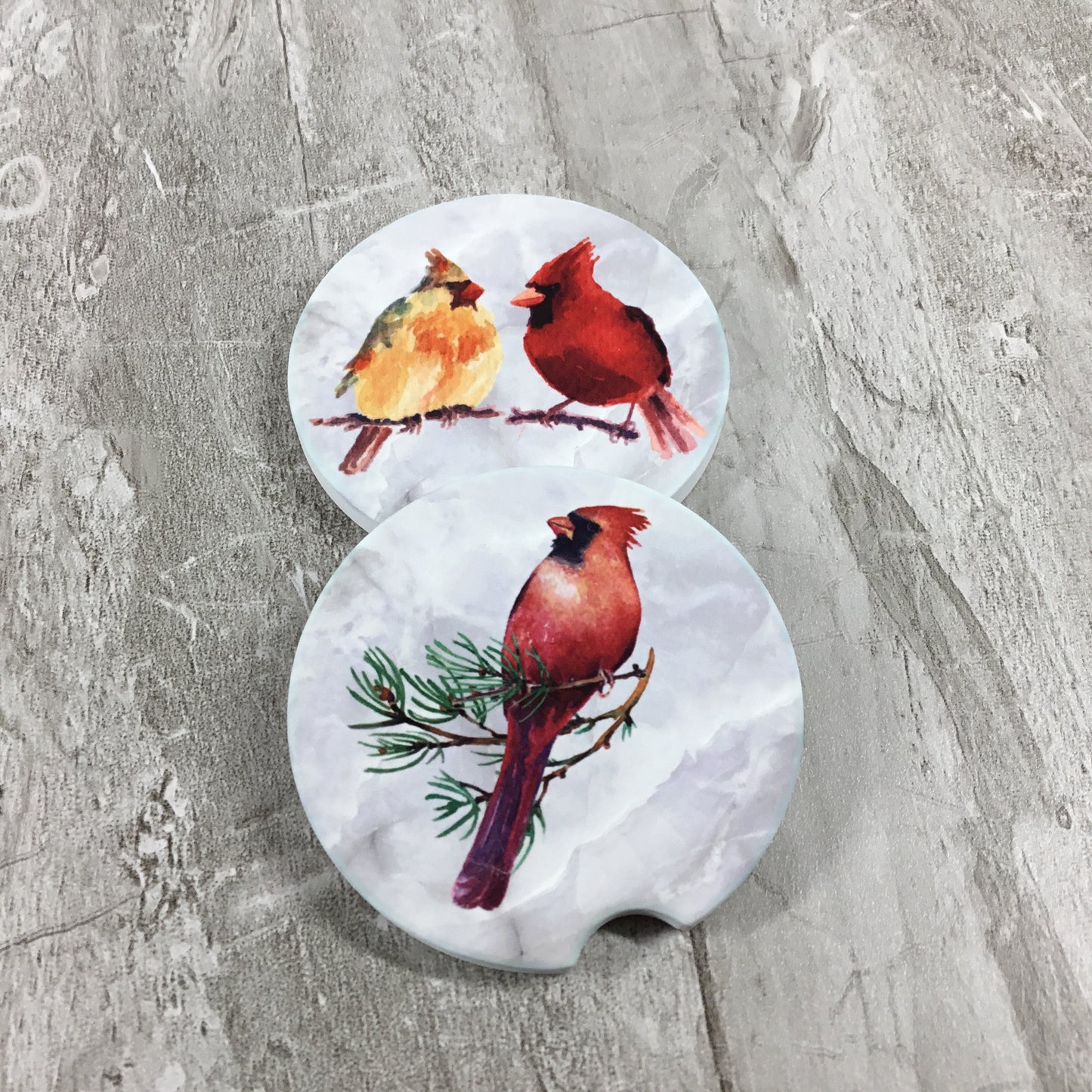 Two car coasters with cardinal bird designs on a gray surface