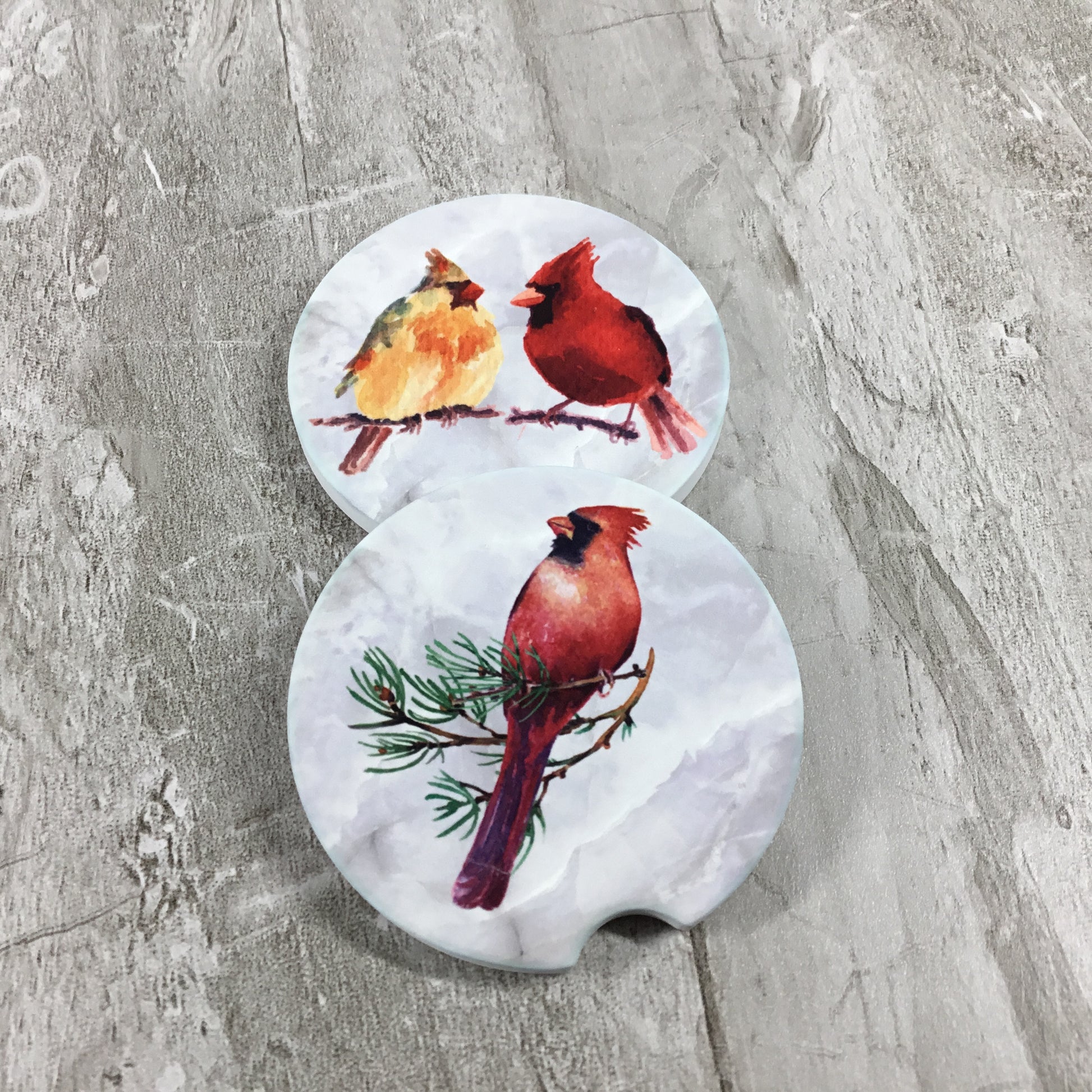 Two car coasters with cardinal bird designs on a gray surface
