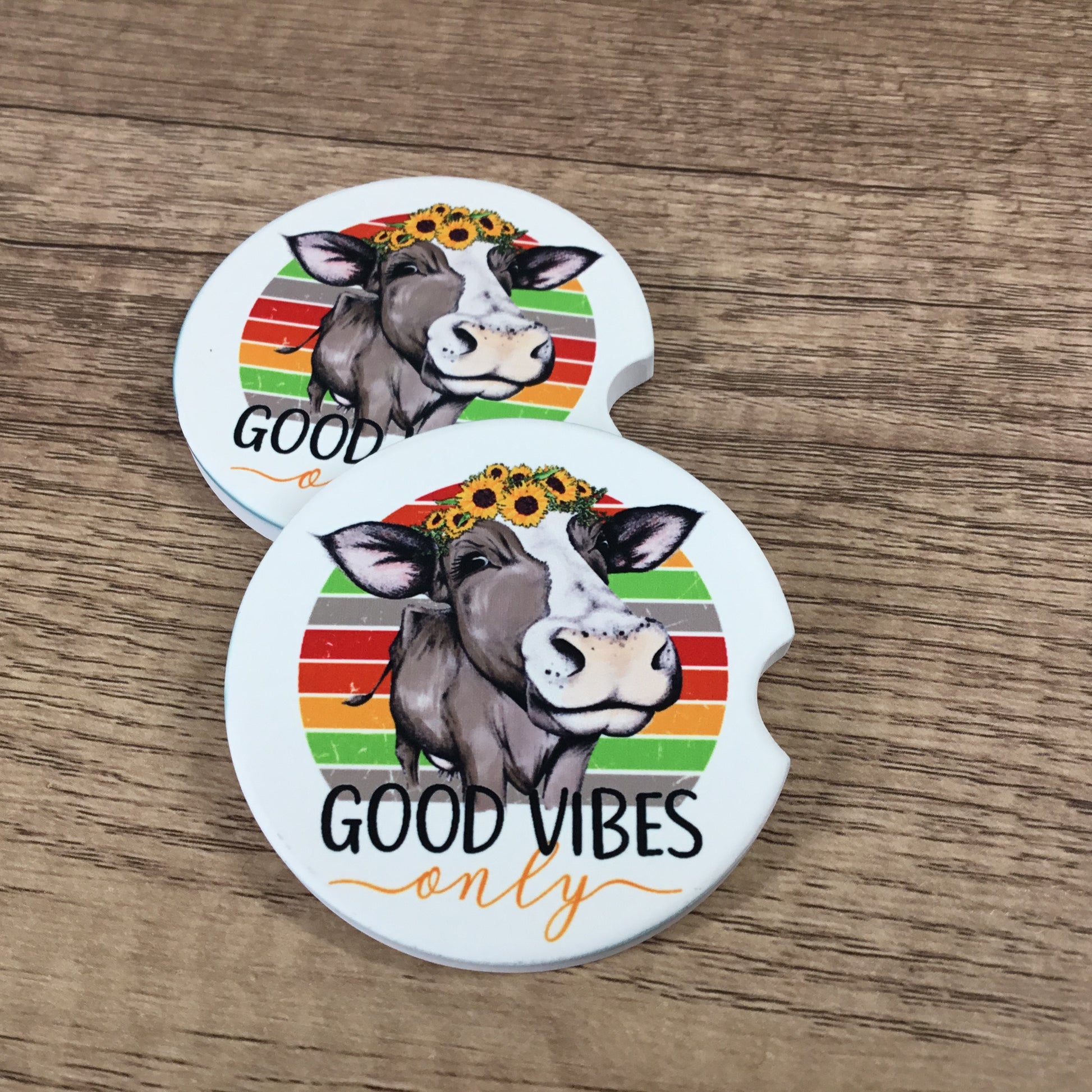 Two car coasters with a cow illustration and 'Good Vibes Only' text on a wooden surface.