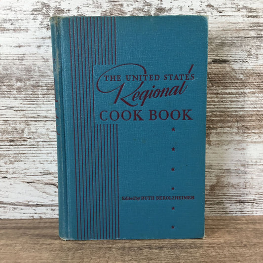 Blue cookbook titled 'The United States Regional Cook Book' on a wooden surface