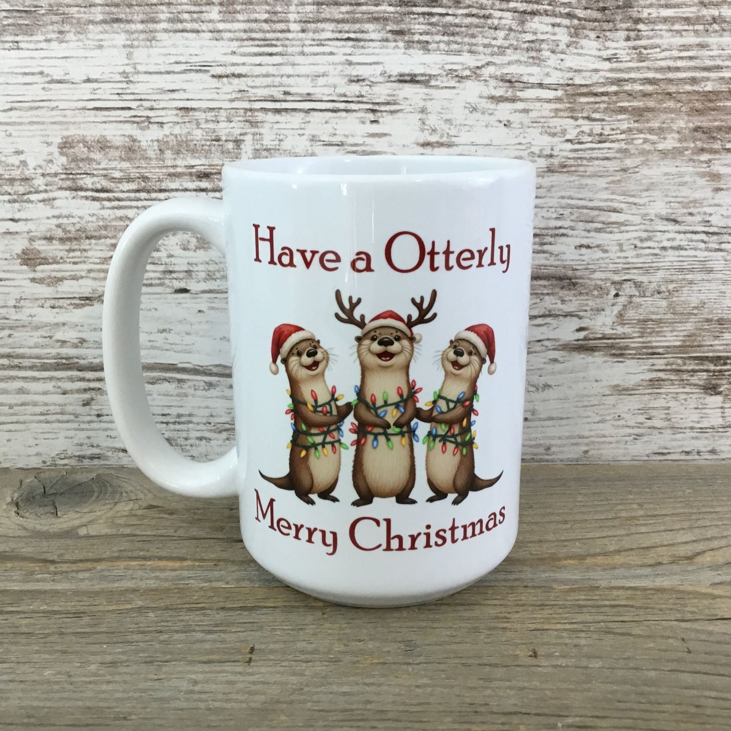 White mug with Christmas-themed design of otters and text on a wooden surface