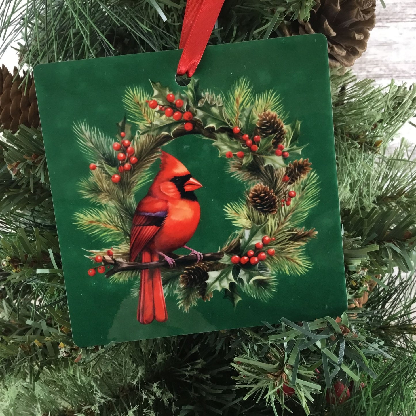 Decorative ornament with a red cardinal bird on a green background, hanging on a Christmas tree.