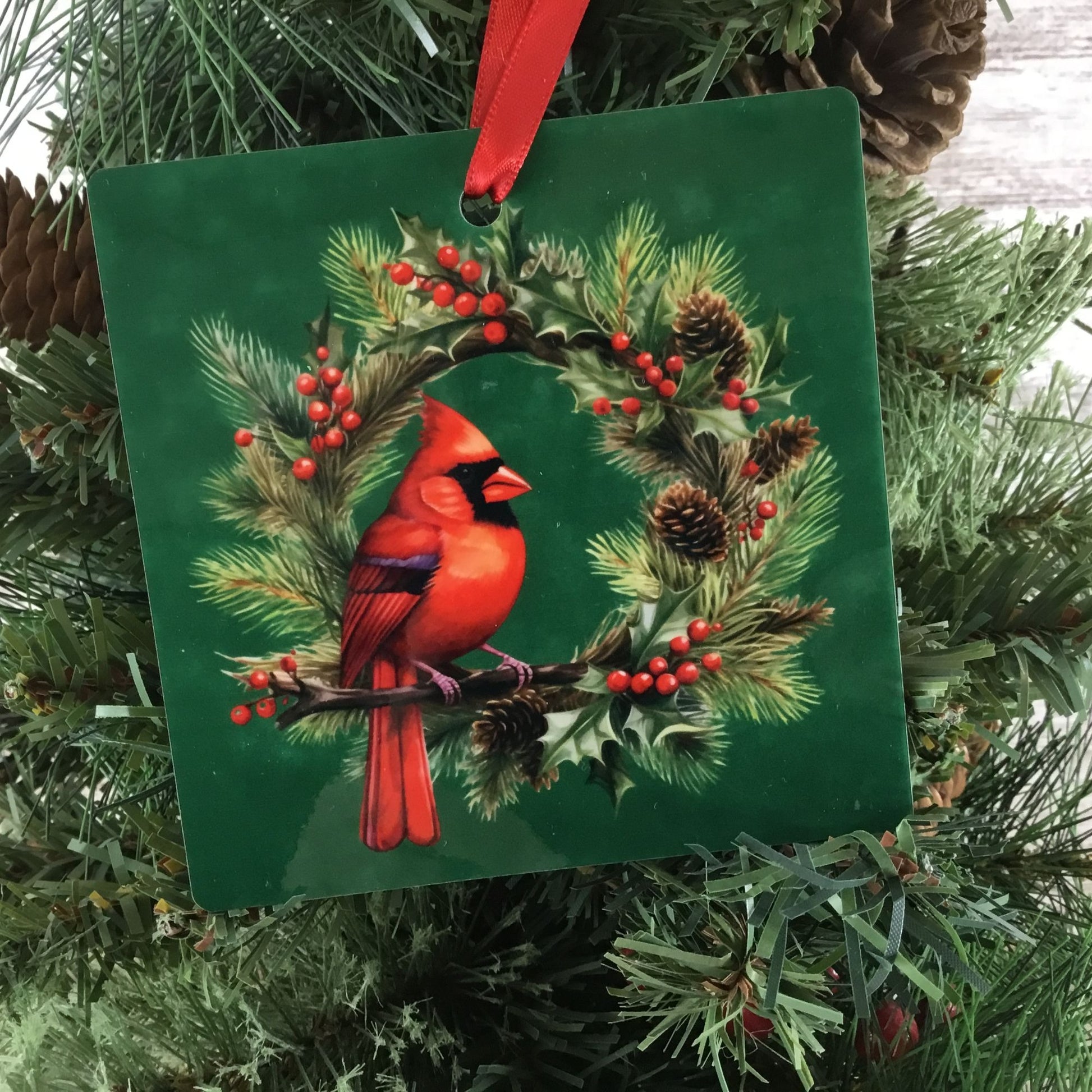 Decorative ornament with a red cardinal bird on a green background, hanging on a Christmas tree.