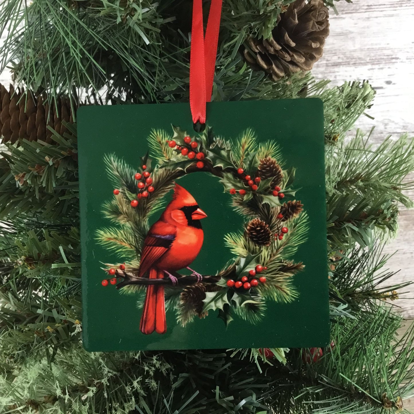 Decorative Christmas ornament with a red cardinal bird on a green background, hanging from a tree.