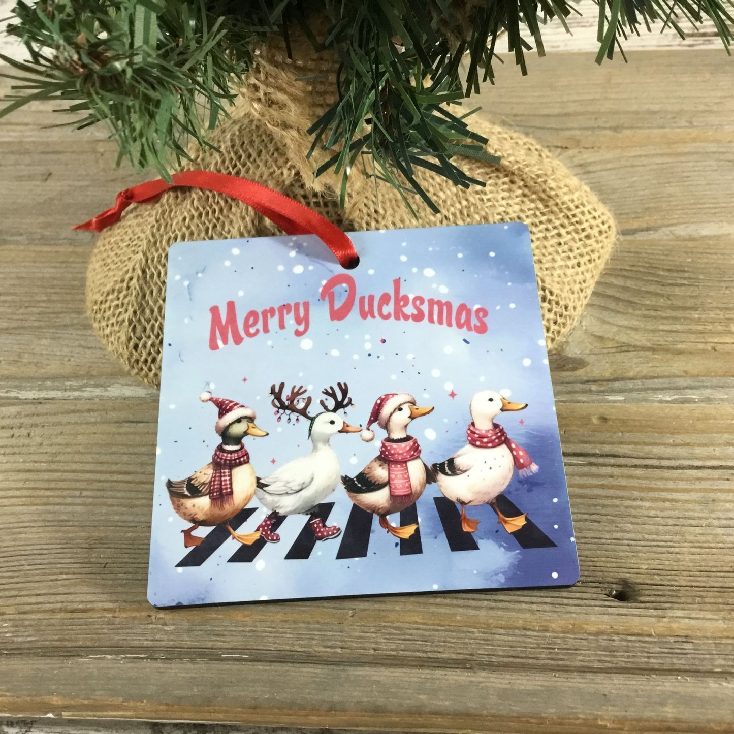 Christmas ornament with ducks crossing a zebra crossing and 'Merry Ducksmas' text, hanging under a tree.