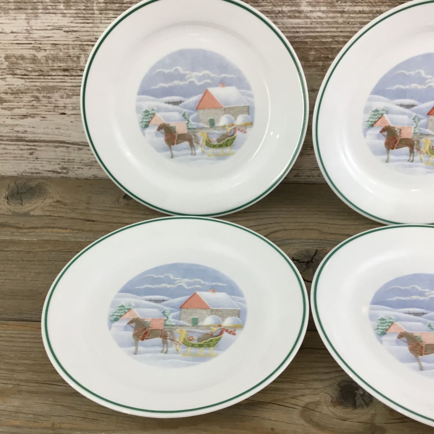 Four ceramic plates with horse and carriage designs on a wooden surface