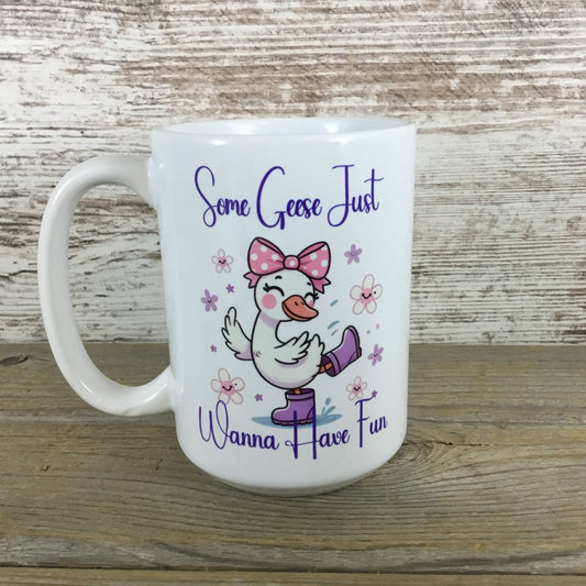 White mug with a cartoon goose wearing a pink bow and purple rain boots, text 'Some Geese Just Wanna Have Fun' on a wooden surface.