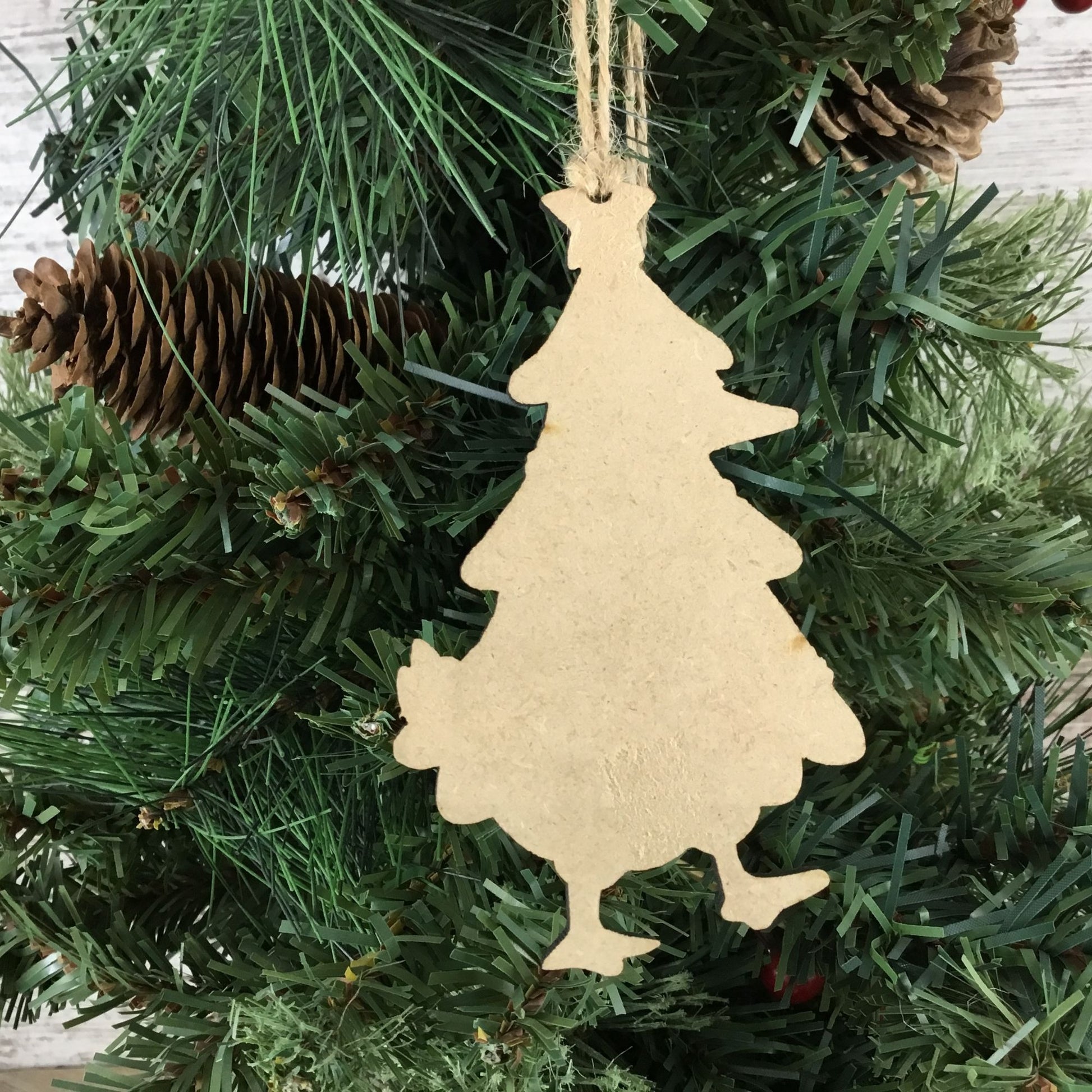 back of Wooden Christmas tree ornament hanging on a green pine branch with pine cones.