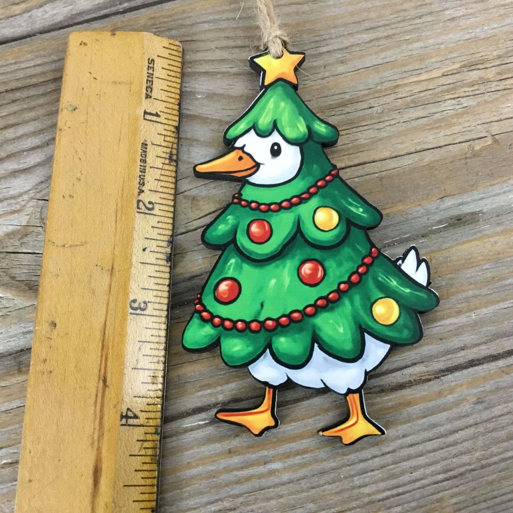 Decorative Christmas tree-shaped ornament with a goose face, hanging on a wooden surface next to a ruler.