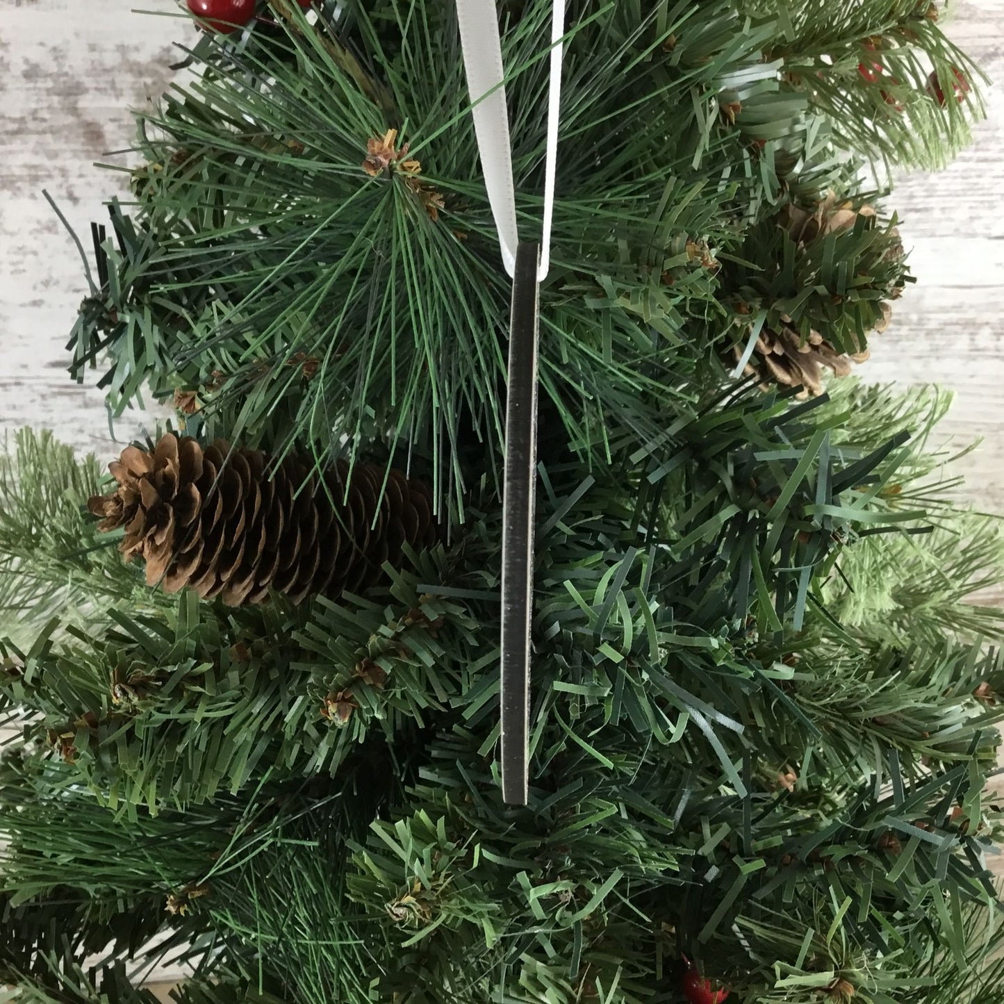 Close-up of a Christmas tree ornament side view with pine cones and a pine needle on a wooden surface.