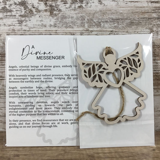A wooden angel-shaped ornament labeled 'Divine Messenger' displayed next to its printed card on a light wood surface. The card includes descriptive text about angels and features a small angel illustration.