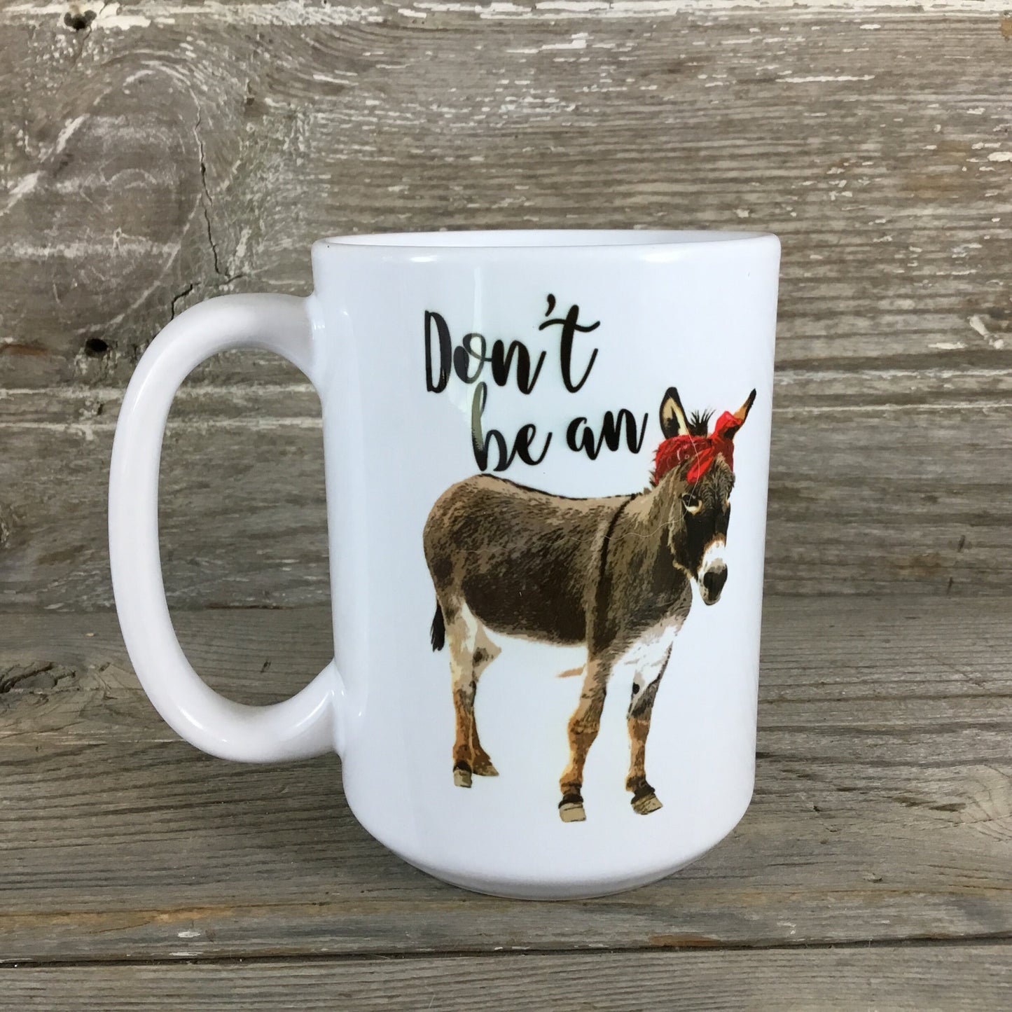 White mug with a donkey illustration and text 'Don't be an' on a wooden background