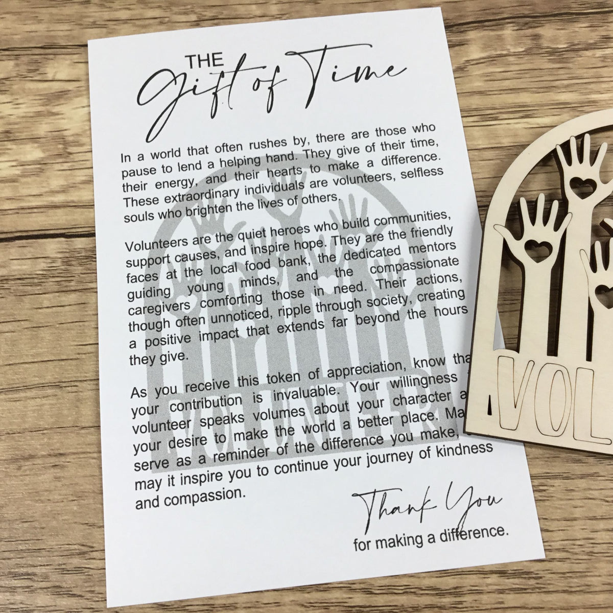 A printed volunteer appreciation card titled 'The Gift of Time' placed on a wooden surface next to a wooden ornament