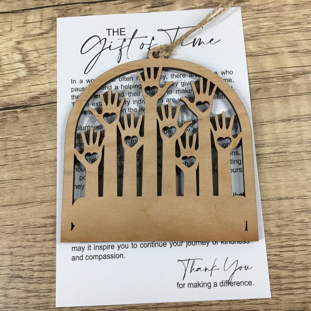 A wooden arched ornament with hand-shaped cutouts hangs from a string over a printed card on a wood surface.