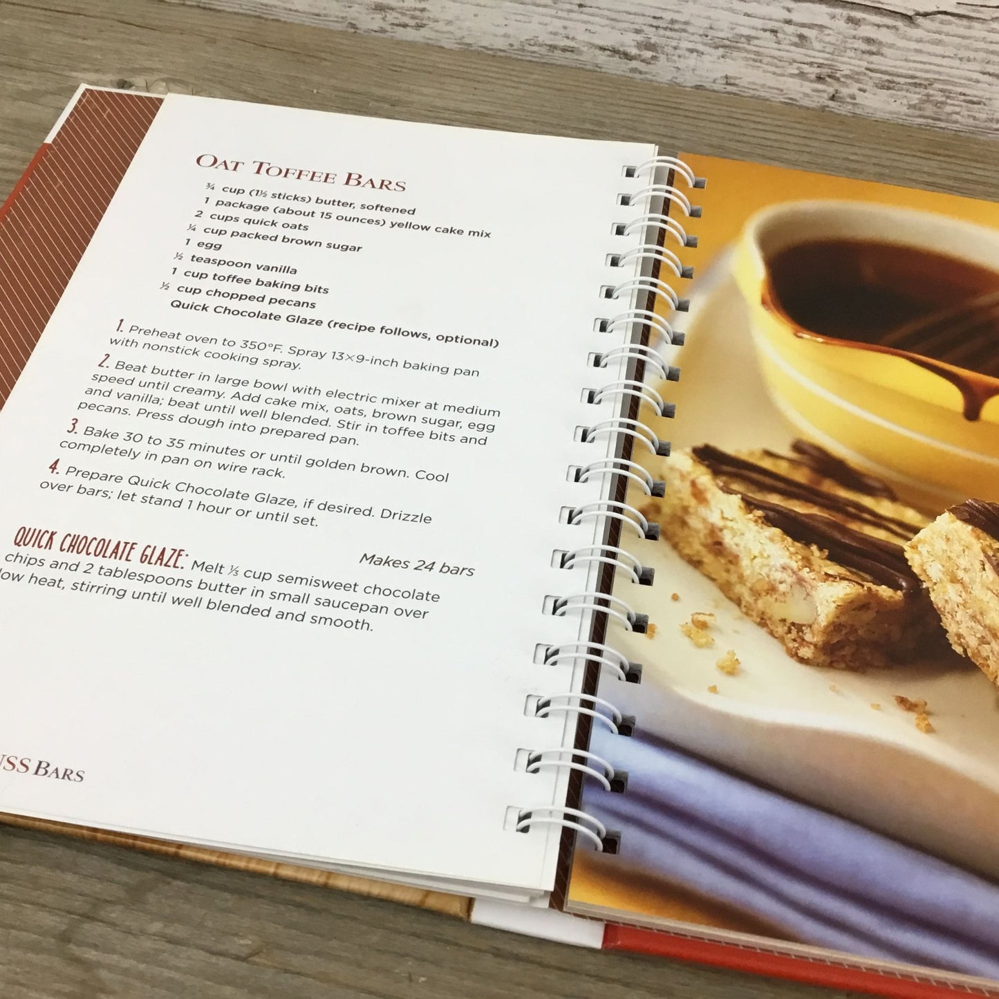 Open cookbook with a recipe for oat toffee bars and a photo of a dessert on a wooden surface.